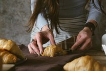 Mani femminili affettare croissant — Foto stock