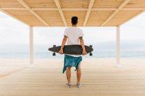 Чоловік зі скейтбордом дивиться на море — стокове фото