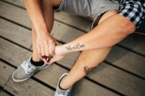 Uomo con tatuaggi seduto sul pavimento in legno — Foto stock