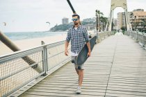Uomo che cammina sul molo con skateboard — Foto stock