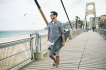 Hombre en ropa de verano caminando con monopatín - foto de stock