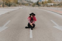 Girl with pink hair in hat sitting on roadway — Stock Photo