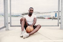 Уверенный человек, сидящий с баскетболом — стоковое фото