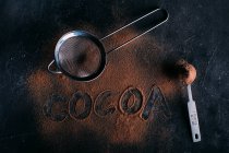 Cacao en poudre et passoire sur fond foncé — Photo de stock