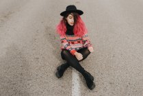 Girl with pink hair in hat sitting on road — Stock Photo