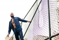 Человек в джинсах позирует на металлическом заборе — стоковое фото