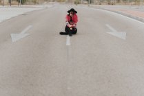 Menina sentada na estrada com pernas cruzadas — Fotografia de Stock