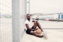 Uomo sicuro seduto con la pallacanestro — Foto stock