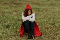 Une fille au chapeau rouge est assise dans une prairie — Photo de stock
