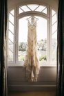 Wedding dress hanging on window — Stock Photo