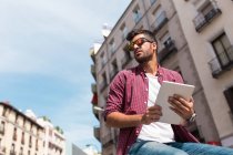 Young handsome man in sunglasses using tablet on urban backgroun — Stock Photo