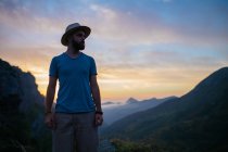Homme au chapeau posant au-dessus du coucher du soleil de montagne — Photo de stock