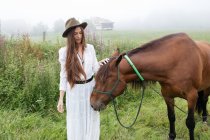 Young girl in white dress stroking horse — Stock Photo