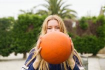 Porträt eines blonden Mädchens, das Gesicht mit Basketballkorb bedeckt und in die Kamera blickt — Stockfoto