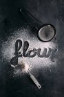 Flour lettering and strainer over dark background — Stock Photo