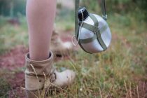 Close up view of tourist flask hanging by female leg at nature — Stock Photo
