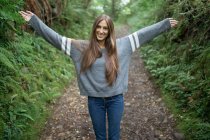 Chica levantando sus brazos en el sendero del bosque - foto de stock