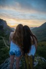 Rückansicht zweier Frauen, die den Sonnenuntergang in den Bergen betrachten — Stockfoto