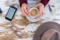 Crop shot from above of female holding phone and coffee on table — Stock Photo