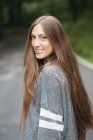 Ritratto di ragazza bruna che indossa un maglione grigio in piedi sulla strada e guarda oltre le spalle la fotocamera — Foto stock