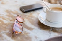 Gros plan de lunettes, téléphone et tasse de café — Photo de stock