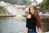 Portrait of young woman with long hair against of river near town — Stock Photo