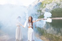 Girls with flares posing at lake — Stock Photo