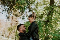 Vista lateral alegre hombre sosteniendo novia en el aire - foto de stock