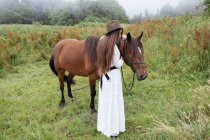 Junges Mädchen im weißen Kleid streichelt Pferd — Stockfoto