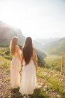 Rückansicht von zwei jungen Freundinnen, die schöne Berglandschaft im Sonnenlicht beobachten. — Stockfoto