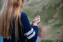 Rückansicht eines Mädchens, das auf den Kompass in der Hand in die Berglandschaft blickt — Stockfoto