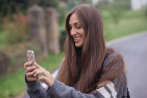 Улыбающаяся женщина с помощью смартфона на дороге в сельской местности — стоковое фото