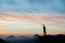 Силуэт женщины, приветствующей закат на вершине горы на фоне удивительного неба — стоковое фото