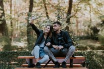 Jeune couple assis sur la table du parc et prenant selfie — Photo de stock