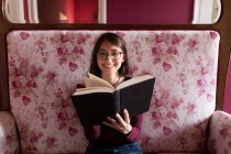 Smiling female with book on couch — Stock Photo