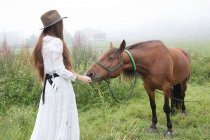 Chica joven en vestido blanco acariciando caballo - foto de stock