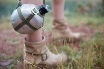 Close-up of touristic flask hanging on strap by female legs — Stock Photo