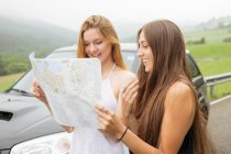 Portrait of two girls standing beside car and looking at map — Stock Photo