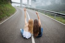 Дві молоді дівчата сидять на гірській дорозі — стокове фото