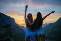 Dos chicas abrazándose sobre el atardecer de montaña - foto de stock