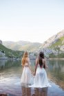 Вид ззаду на номен у білих сукнях, що стоять у гірському озері — стокове фото