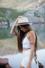 Retrato de mujer morena feliz en sombrero posando contra de lago de montaña - foto de stock