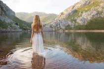 Visão traseira da mulher de pé no lago da montanha em vestido branco — Fotografia de Stock
