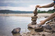 Male hands making stone tower at shore on cloudy day — Stock Photo