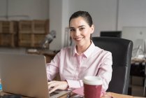 Smiling business woman browsing laptop at workplace and looking at camera — Stock Photo