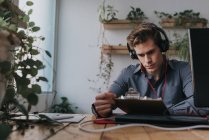 Portrait of man wearing headphones sitting at workplace and looking at clipboard — Stock Photo