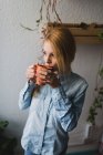 Retrato de chica rubia bebiendo taza de té y mirando a la ventana - foto de stock