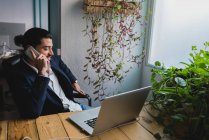 Retrato de homem de negócios sentado no local de trabalho com laptop e conversando por telefone — Fotografia de Stock