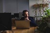 Retrato de hombre en auriculares sentado en la mesa con el ordenador portátil y mirando hacia otro lado - foto de stock