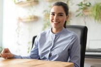 Lächelnde Geschäftsfrau sitzt am Arbeitsplatz im Bürostuhl und blickt in die Kamera — Stockfoto